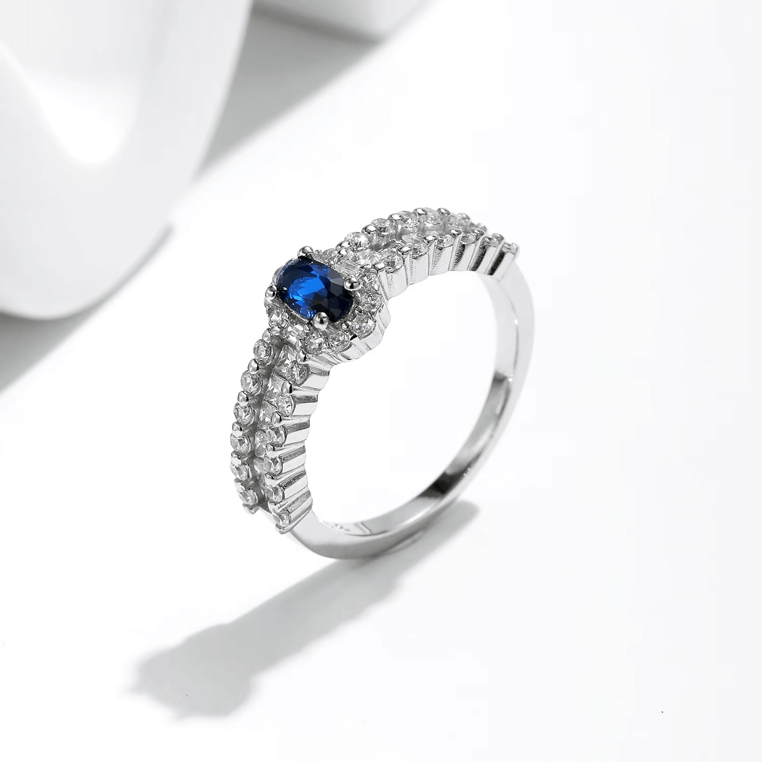 925 sterling silver ring featuring a deep blue oval sapphire and a triple row of shimmering zirconia stones, styled on hand and in detail