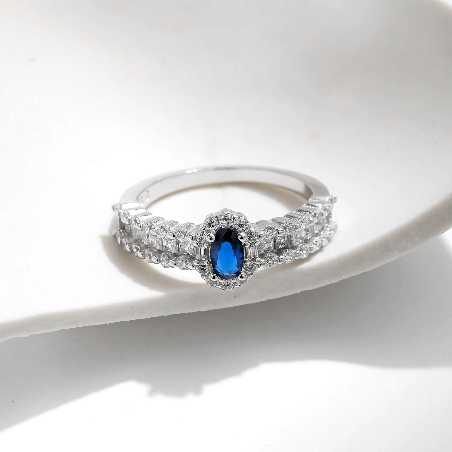 925 sterling silver ring featuring a deep blue oval sapphire and a triple row of shimmering zirconia stones, styled on hand and in detail